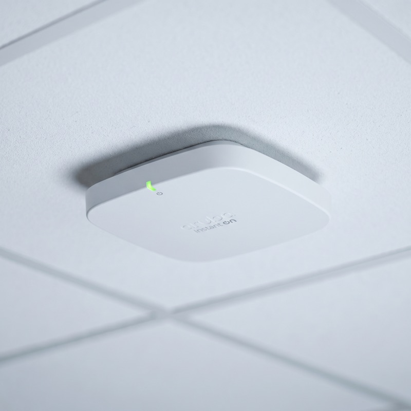 White Aruba Instant On AP-515 wireless access point mounted on a ceiling tile